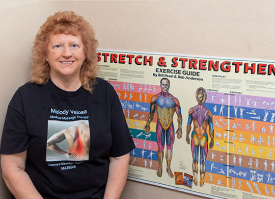 Melody Martin Velosa Medical Massage therapist: Standing near a "Stretch & Strengthen" wall chart